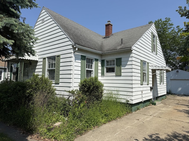 911 Napier Ave, Saint Joseph, MI 49085 - view of side of home featuring a chimney, a shingled roof, an outdoor structure, a detached garage, and concrete driveway