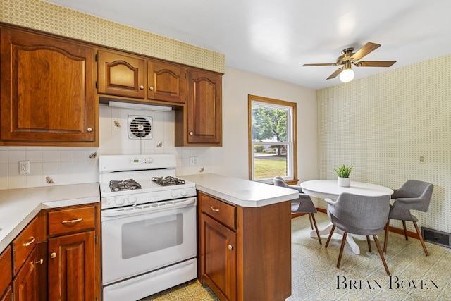 1665 7th St NW, Grand Rapids, MI 49504 - kitchen featuring white range with gas cooktop, a peninsula, light countertops, ceiling fan, and wallpapered walls