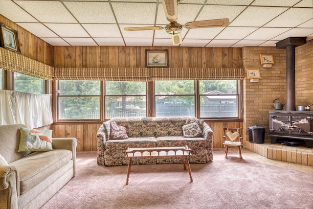 8182 Hardy Dr, Newaygo, MI 49337 - living area featuring a wood stove, wood walls, a ceiling fan, carpet floors, and a paneled ceiling