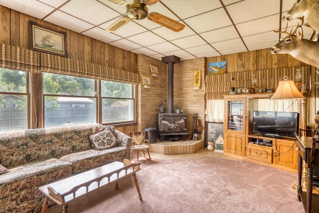 8182 Hardy Dr, Newaygo, MI 49337 - carpeted living area with wooden walls, a wood stove, ceiling fan, and a paneled ceiling