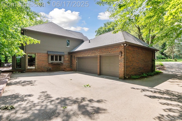 2020 Pine Hollow Trl, Brighton, MI 48114 - view of side of property featuring brick siding, a garage, asphalt driveway, and roof with shingles