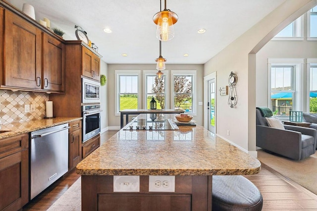 2753 Colton Dr, Berrien Springs, MI 49103 - kitchen with stainless steel appliances, decorative backsplash, light stone countertops, a center island, and decorative light fixtures