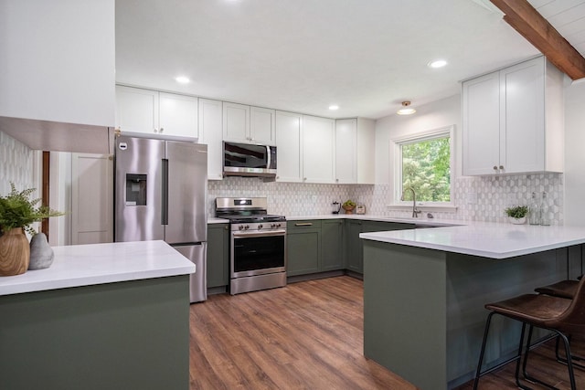 3737 Peach Ridge Ave NW, Grand Rapids, MI 49544 - kitchen with stainless steel appliances, a peninsula, a breakfast bar area, backsplash, and dark wood-style floors