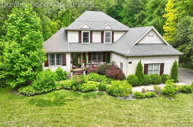 115 Audubon Dr, White Lake, MI 48383 - traditional-style home with covered porch, a front yard, roof with shingles, and brick siding
