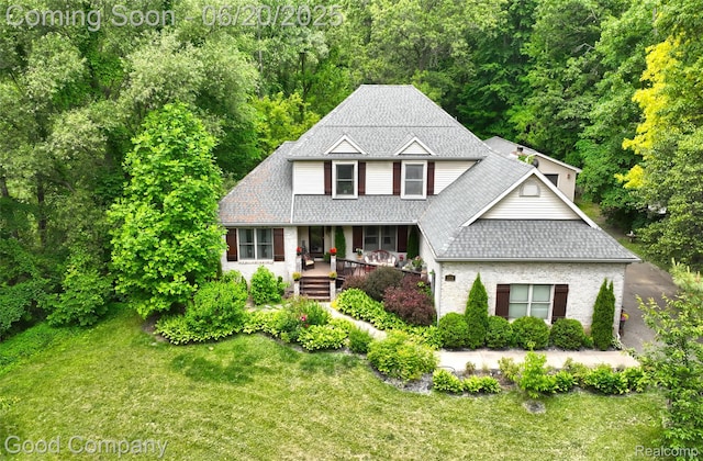 115 Audubon Dr, White Lake, MI 48383 - traditional-style house featuring a porch, a front yard, roof with shingles, brick siding, and a view of trees