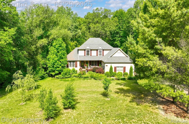 115 Audubon Dr, White Lake, MI 48383 - traditional-style house with a front yard, covered porch, and a view of trees