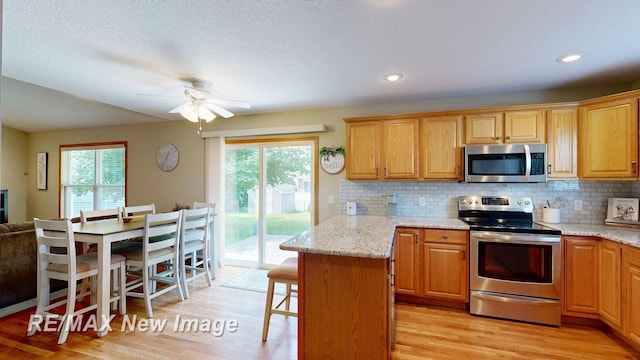 3137 Sundown Ln, Saginaw, MI 48603 - kitchen with stainless steel appliances, light wood-style floors, a ceiling fan, a breakfast bar area, and decorative backsplash