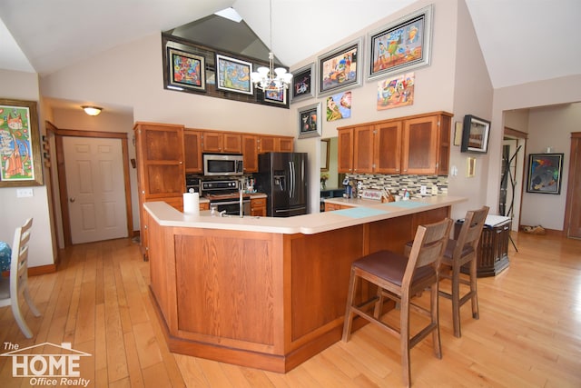 2411 Escott Rd, Owosso, MI 48867 - kitchen featuring appliances with stainless steel finishes, high vaulted ceiling, a peninsula, light countertops, and brown cabinets
