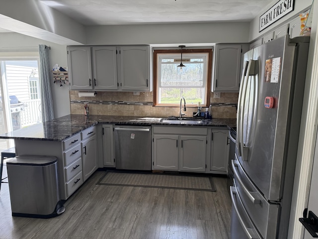 11199 Edgewood Rd, Bellevue, MI 49021 - kitchen with stainless steel appliances, a peninsula, dark wood-style flooring, backsplash, and dark stone counters