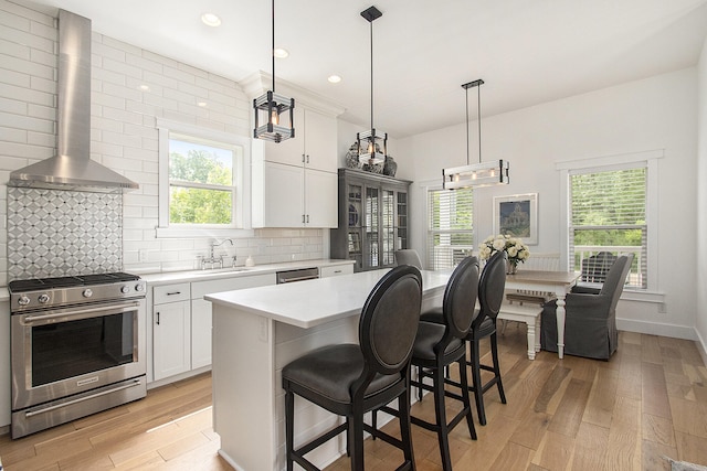 7285 Maple St, South Haven, MI 49090 - kitchen featuring stainless steel gas stove, wall chimney range hood, light countertops, light wood finished floors, and tasteful backsplash