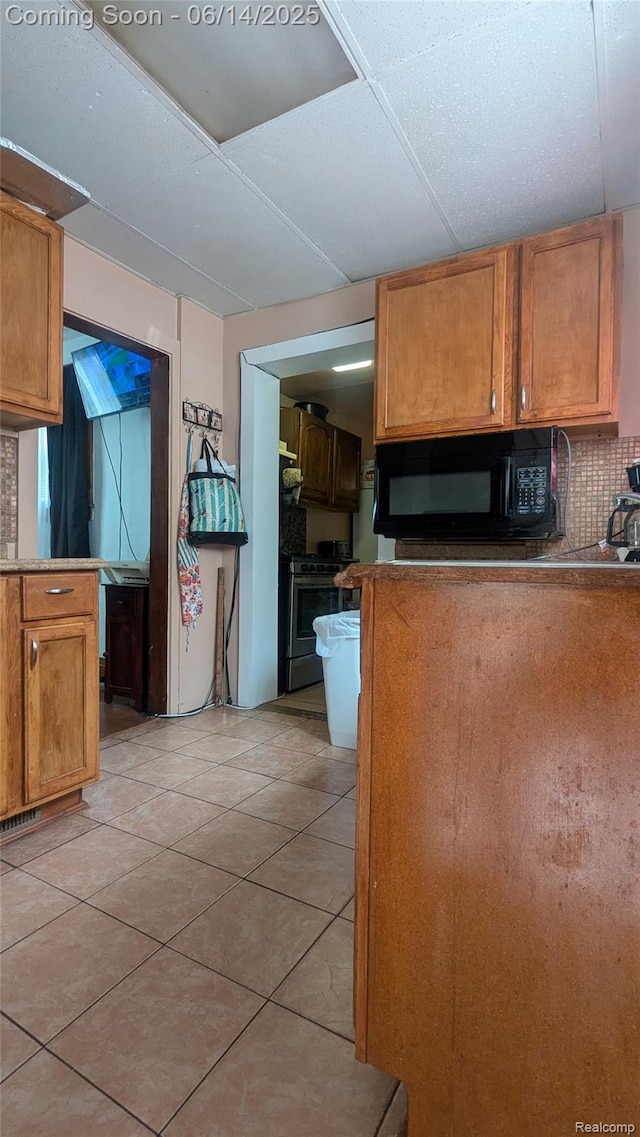 100 Oliver St, Pontiac, MI 48342 - kitchen featuring black microwave, stainless steel gas stove, light tile patterned flooring, decorative backsplash, and brown cabinetry