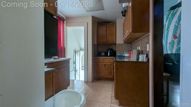 100 Oliver St, Pontiac, MI 48342 - kitchen featuring backsplash, brown cabinetry, light tile patterned floors, a drop ceiling, and dark countertops