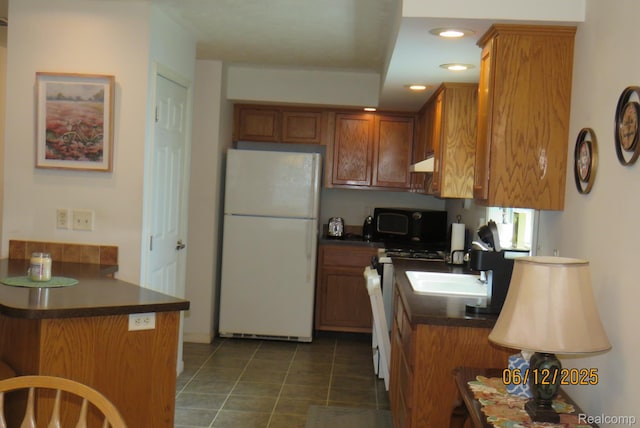 10571 Baraga St, Taylor, MI 48180 - kitchen with freestanding refrigerator, gas range, dark countertops, brown cabinets, and under cabinet range hood