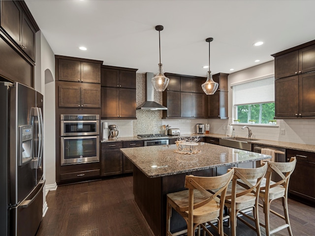 13531 Brampton Ct, Utica, MI 48315 - kitchen with appliances with stainless steel finishes, wall chimney range hood, dark brown cabinets, dark wood-style flooring, and a kitchen bar