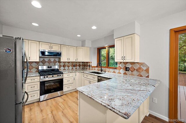 2696 Cedar Key Dr, Lake Orion, MI 48360 - kitchen with appliances with stainless steel finishes, cream cabinets, light wood-type flooring, a peninsula, and healthy amount of natural light