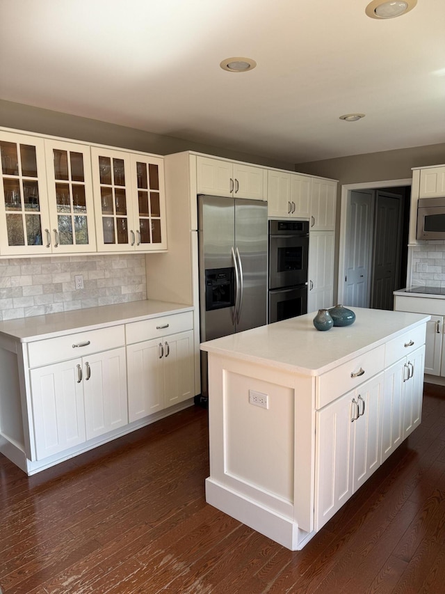 5653 Powder Horn Dr, West Bloomfield, MI 48322 - kitchen featuring appliances with stainless steel finishes, decorative backsplash, glass insert cabinets, dark wood finished floors, and white cabinetry