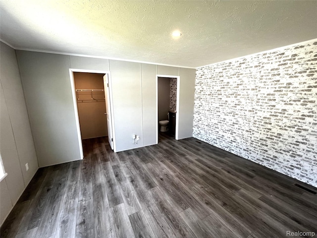 1048 Pheasant Dr, Bay City, MI 48706 - unfurnished bedroom featuring dark wood-style floors, a walk in closet, a textured ceiling, a closet, and crown molding