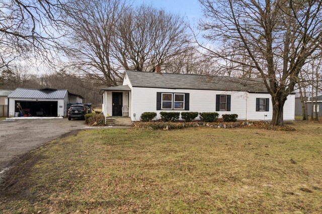 10765 Northland Dr, Big Rapids, MI 49307 - view of front facade featuring an outdoor structure, a detached garage, a front lawn, a chimney, and driveway