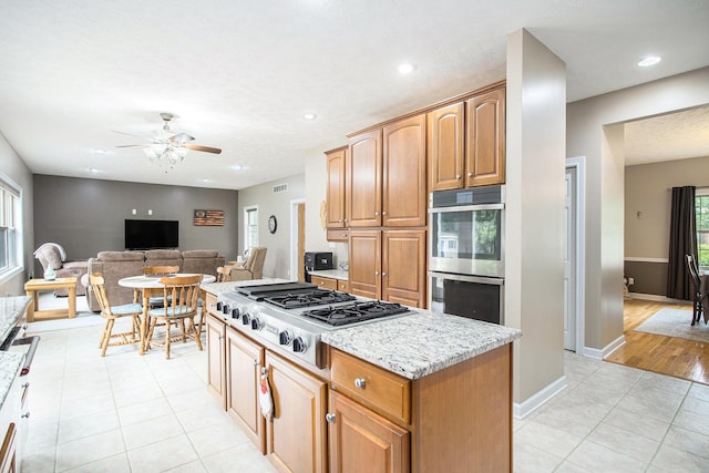 17872 Victors Ln, Marshall, MI 49068 - kitchen with stainless steel appliances, a ceiling fan, light tile patterned floors, light stone countertops, and a kitchen island