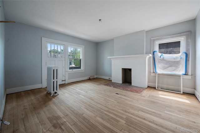 69 Massachusetts St, Highland Park, MI 48203 - unfurnished living room with radiator, light wood-style flooring, and a fireplace