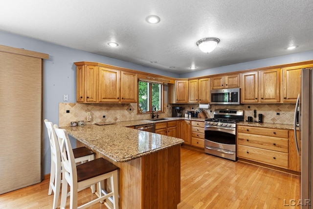 838 Stetson St, Tecumseh, MI 49286 - kitchen with stainless steel appliances, a peninsula, light wood-style floors, decorative backsplash, and a kitchen bar