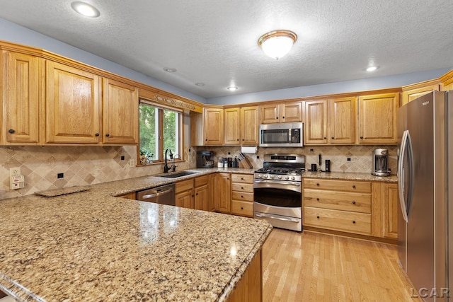 838 Stetson St, Tecumseh, MI 49286 - kitchen featuring stainless steel appliances, a peninsula, light stone countertops, light wood finished floors, and a textured ceiling