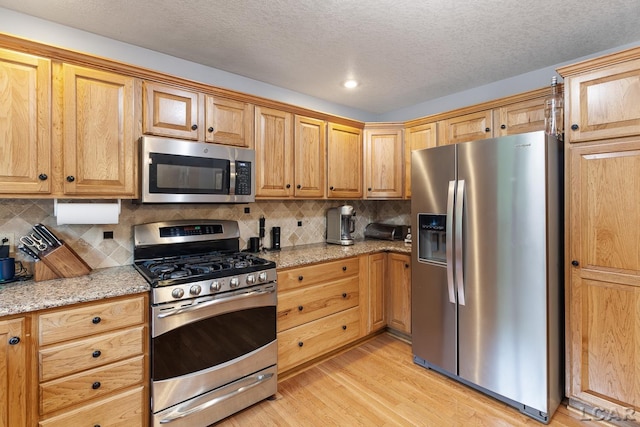 838 Stetson St, Tecumseh, MI 49286 - kitchen with stainless steel appliances, light wood-style flooring, tasteful backsplash, light stone counters, and a textured ceiling