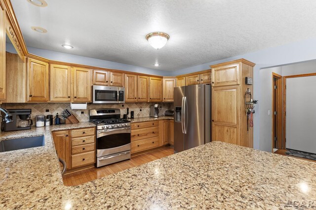 838 Stetson St, Tecumseh, MI 49286 - kitchen featuring appliances with stainless steel finishes, backsplash, light stone counters, light wood finished floors, and a textured ceiling