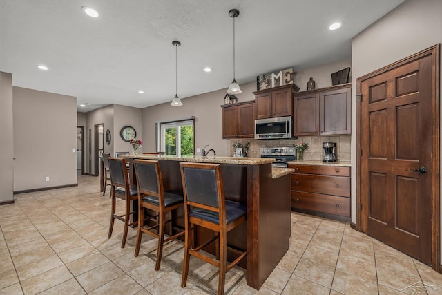 11619 Saddlebrook Cir, Freeland, MI 48623 - kitchen featuring appliances with stainless steel finishes, backsplash, a center island with sink, dark brown cabinetry, and a kitchen bar