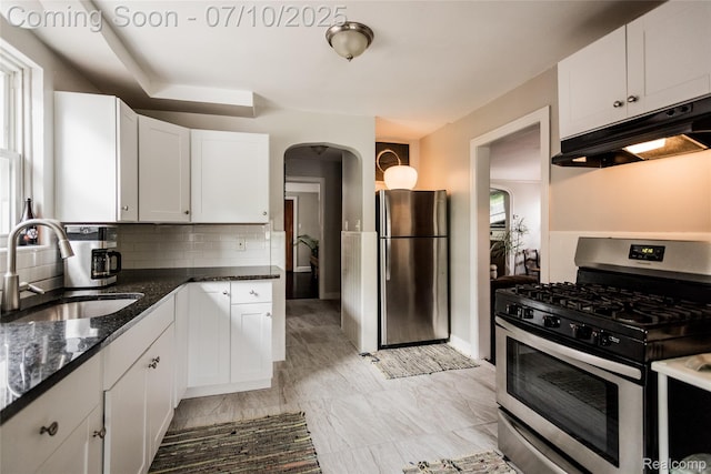 3924 Yorkshire Rd, Detroit, MI 48224 - kitchen with appliances with stainless steel finishes, under cabinet range hood, arched walkways, dark stone counters, and decorative backsplash