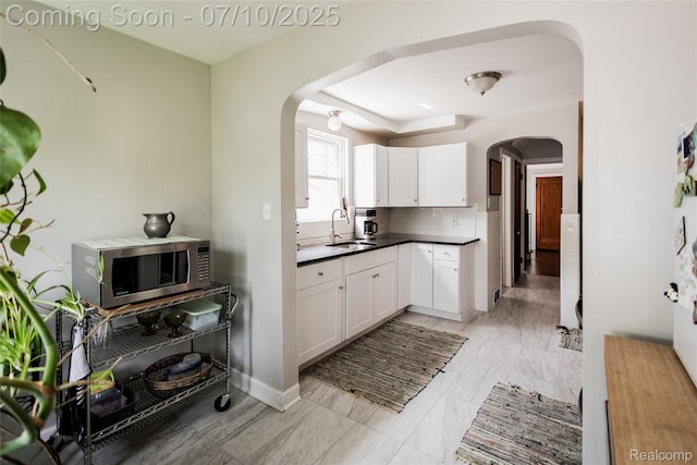 3924 Yorkshire Rd, Detroit, MI 48224 - kitchen featuring arched walkways, stainless steel microwave, white cabinetry, and backsplash