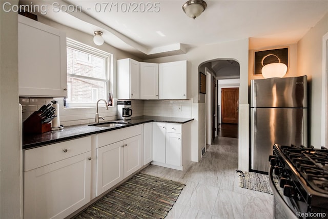 3924 Yorkshire Rd, Detroit, MI 48224 - kitchen with black gas range oven, tasteful backsplash, arched walkways, white cabinets, and freestanding refrigerator