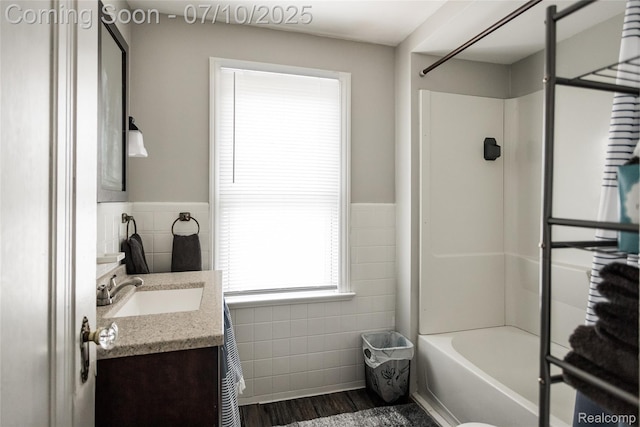 3924 Yorkshire Rd, Detroit, MI 48224 - bathroom featuring tile walls, vanity, a wainscoted wall, washtub / shower combination, and wood finished floors