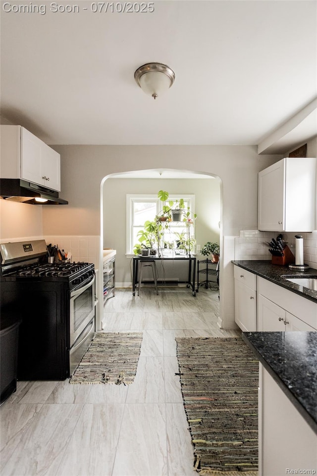 3924 Yorkshire Rd, Detroit, MI 48224 - kitchen with stainless steel gas range oven, under cabinet range hood, arched walkways, white cabinetry, and dark stone countertops
