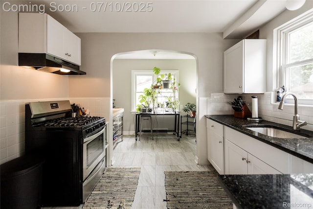3924 Yorkshire Rd, Detroit, MI 48224 - kitchen with stainless steel range with gas cooktop, under cabinet range hood, arched walkways, dark stone counters, and white cabinetry