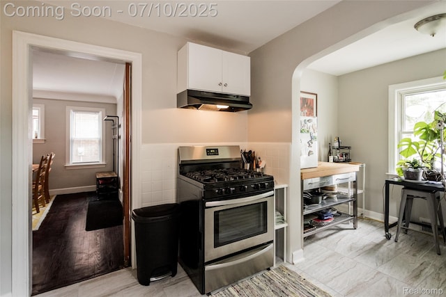 3924 Yorkshire Rd, Detroit, MI 48224 - kitchen with under cabinet range hood, gas stove, white cabinetry, arched walkways, and tile walls