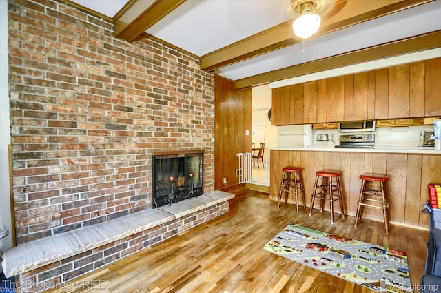 1038 Cora Dr, Flint, MI 48532 - kitchen with stainless steel appliances, beamed ceiling, wood finished floors, ceiling fan, and a brick fireplace