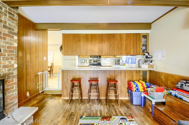 1038 Cora Dr, Flint, MI 48532 - kitchen featuring stainless steel appliances, wood finished floors, a kitchen breakfast bar, brown cabinetry, and wood walls