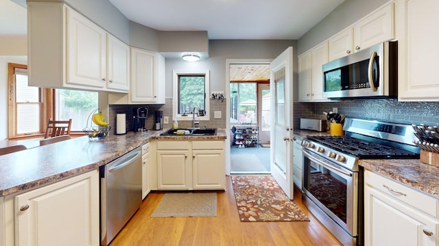 10 Covell Ave NW, Grand Rapids, MI 49504 - kitchen featuring appliances with stainless steel finishes, tasteful backsplash, light wood-style floors, and white cabinetry