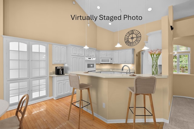 6916 Windsong Way, Kalamazoo, MI 49009 - kitchen with white appliances, high vaulted ceiling, a peninsula, a breakfast bar, and light countertops