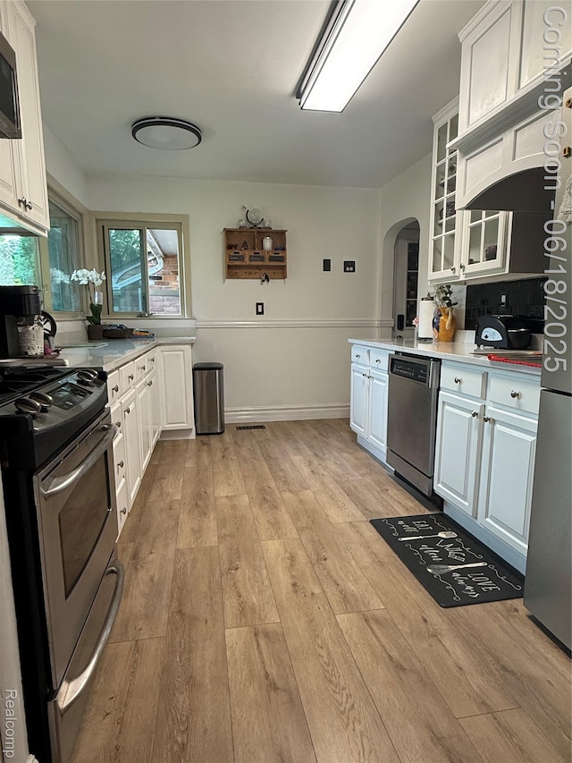 6715 Elizabeth Lake Rd, Waterford, MI 48327 - kitchen with stainless steel appliances, arched walkways, white cabinetry, light wood-type flooring, and light countertops