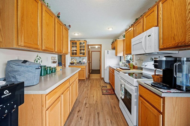 66291 M-62, Edwardsburg, MI 49112 - kitchen featuring white appliances, light wood-style flooring, light countertops, brown cabinetry, and glass insert cabinets