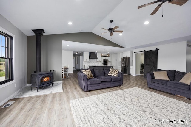 1153 S Edgar Rd, Mason, MI 48854 - living room featuring a barn door, a ceiling fan, a wood stove, lofted ceiling, and light wood-type flooring