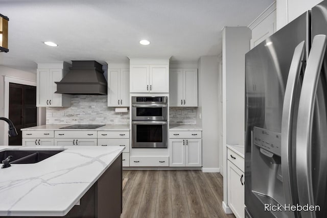 1153 S Edgar Rd, Mason, MI 48854 - kitchen featuring appliances with stainless steel finishes, custom range hood, wood finished floors, white cabinetry, and decorative backsplash