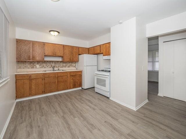 1314 Magnolia St, Kalamazoo, MI 49048 - kitchen featuring white appliances, brown cabinets, light wood-style flooring, light countertops, and exhaust hood