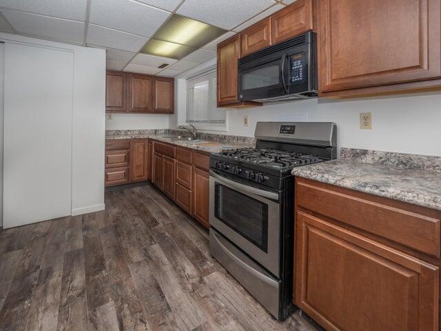 1516 Nazareth Rd, Kalamazoo, MI 49048 - kitchen with stainless steel gas stove, black microwave, dark wood finished floors, brown cabinets, and a paneled ceiling