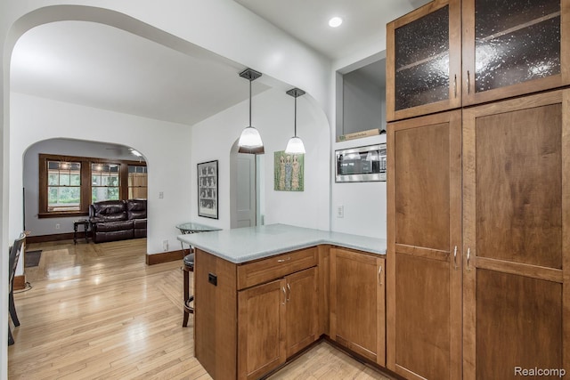 284 W Clarkston Rd, Lake Orion, MI 48362 - kitchen with arched walkways, brown cabinets, a peninsula, light wood finished floors, and glass insert cabinets