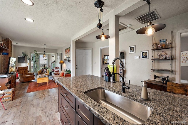 1769 W Warren Ave, Detroit, MI 48208 - kitchen featuring a textured ceiling, light wood finished floors, dark stone countertops, decorative light fixtures, and open floor plan