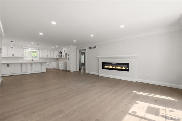56350 Willow Creek Blvd, Utica, MI 48316 - unfurnished living room with ornamental molding, recessed lighting, light wood-type flooring, and a glass covered fireplace