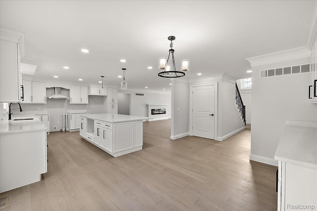 56350 Willow Creek Blvd, Utica, MI 48316 - kitchen with crown molding, wall chimney exhaust hood, recessed lighting, white cabinetry, and light wood-style flooring